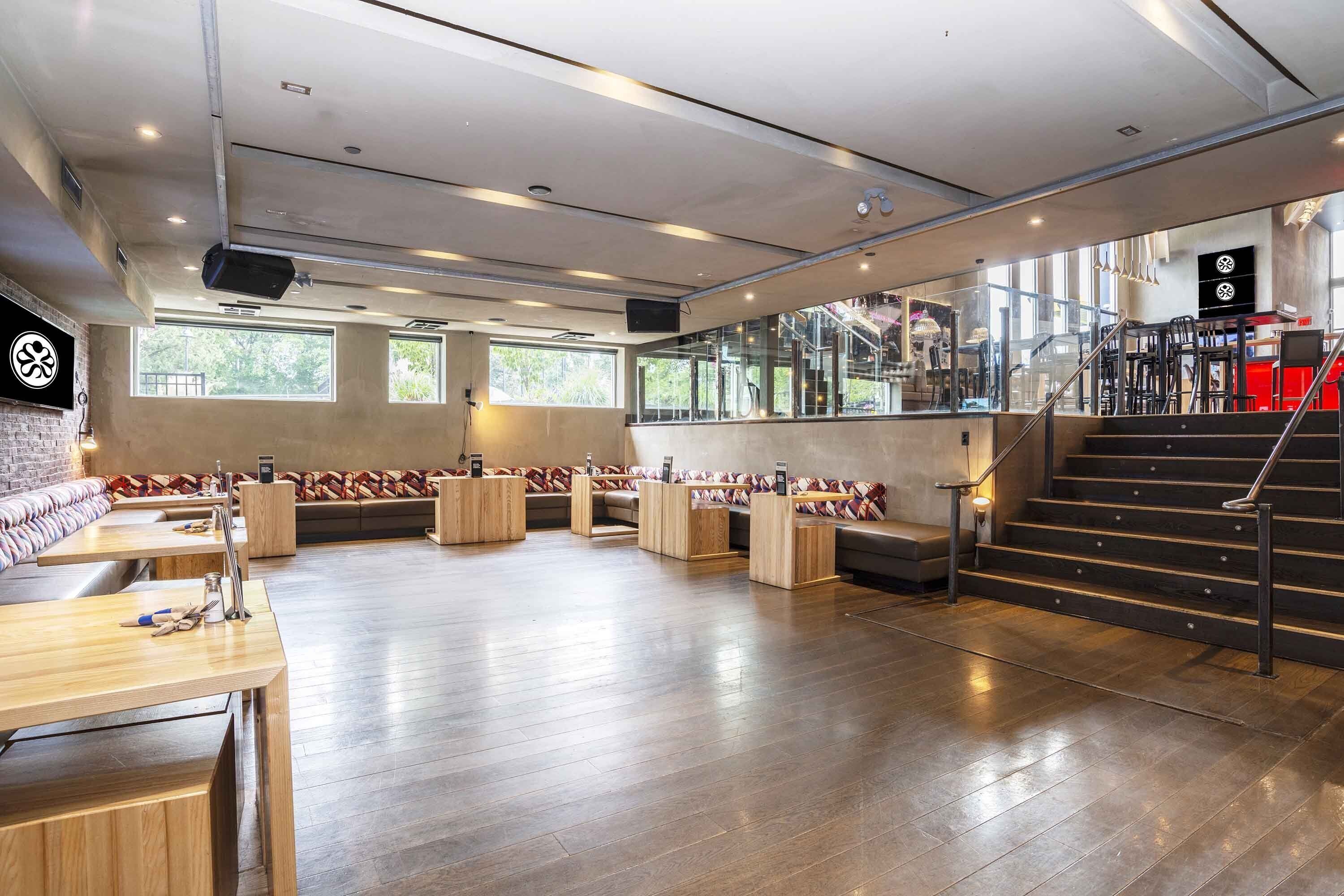 A spacious lobby with wooden flooring, seating areas, a staircase, and large windows.