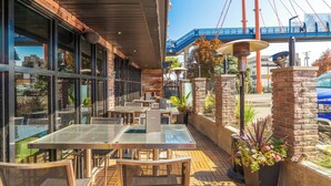 An outdoor patio with tables and chairs, a brick wall, and a view of a bridge. - Sandman Signature Kamloops Hotel (Kamloops)