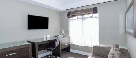 Habitación de hotel con escritorio, silla y un amplio ventanal con cortinas.