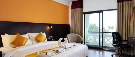 A hotel room with a large bed, a desk with a chair, and a view of the outdoors through a sliding door.