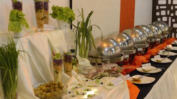 A buffet table with various food items and salad bowls, accompanied by a large metal serving pot and a potted plant.