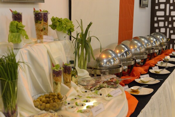 A buffet table with various food items and salad bowls, accompanied by a large metal serving pot and a potted plant. - ASTORIA HOTELS MADURAI (Madurai)