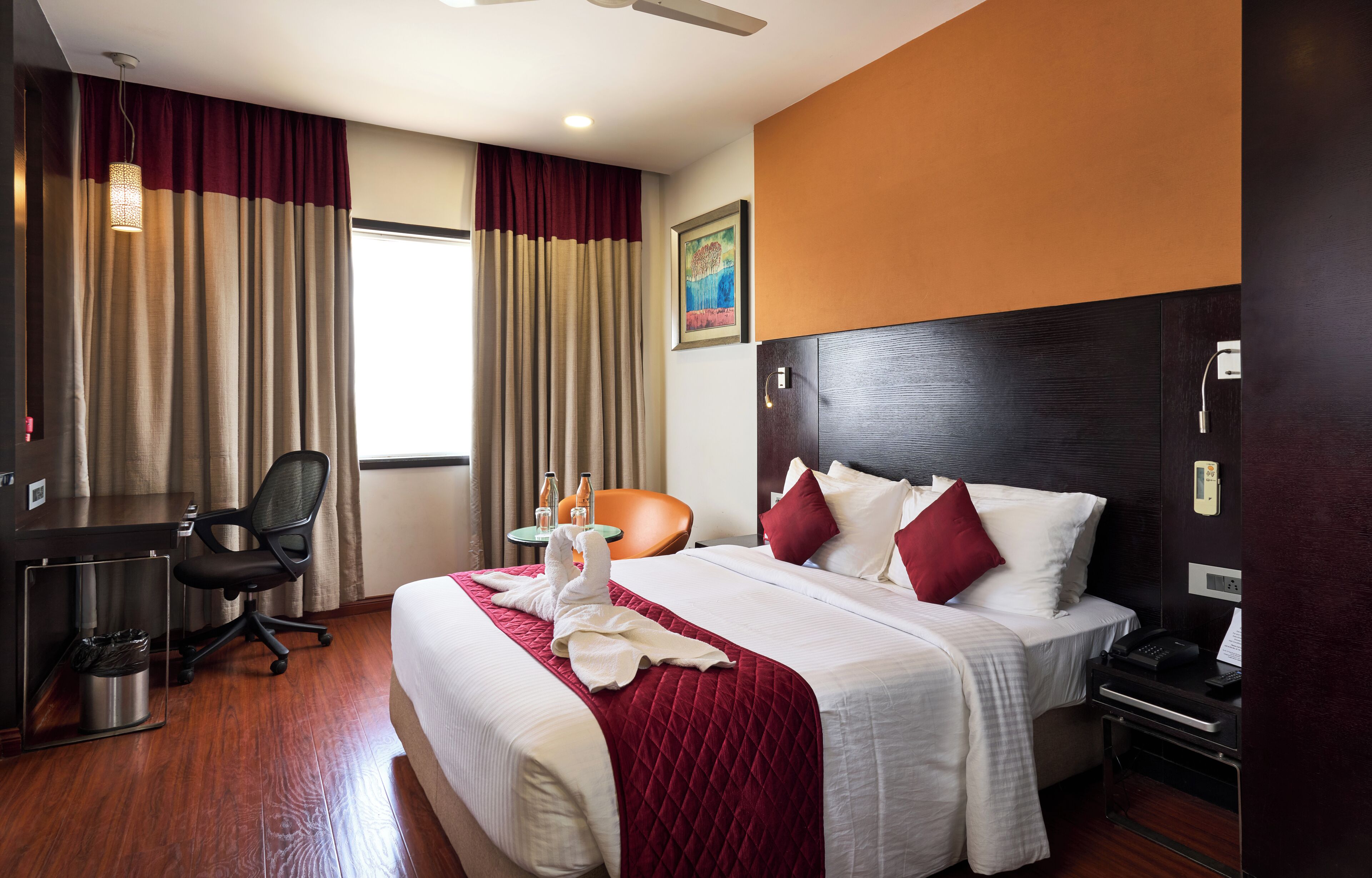 A hotel room with a bed, desk, chair, and a small table with bottles.