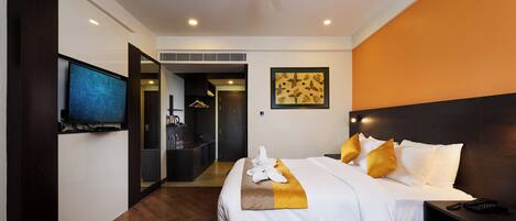 A modern hotel room with a large bed, a flat-screen TV, a ceiling fan, and a view into the hallway.