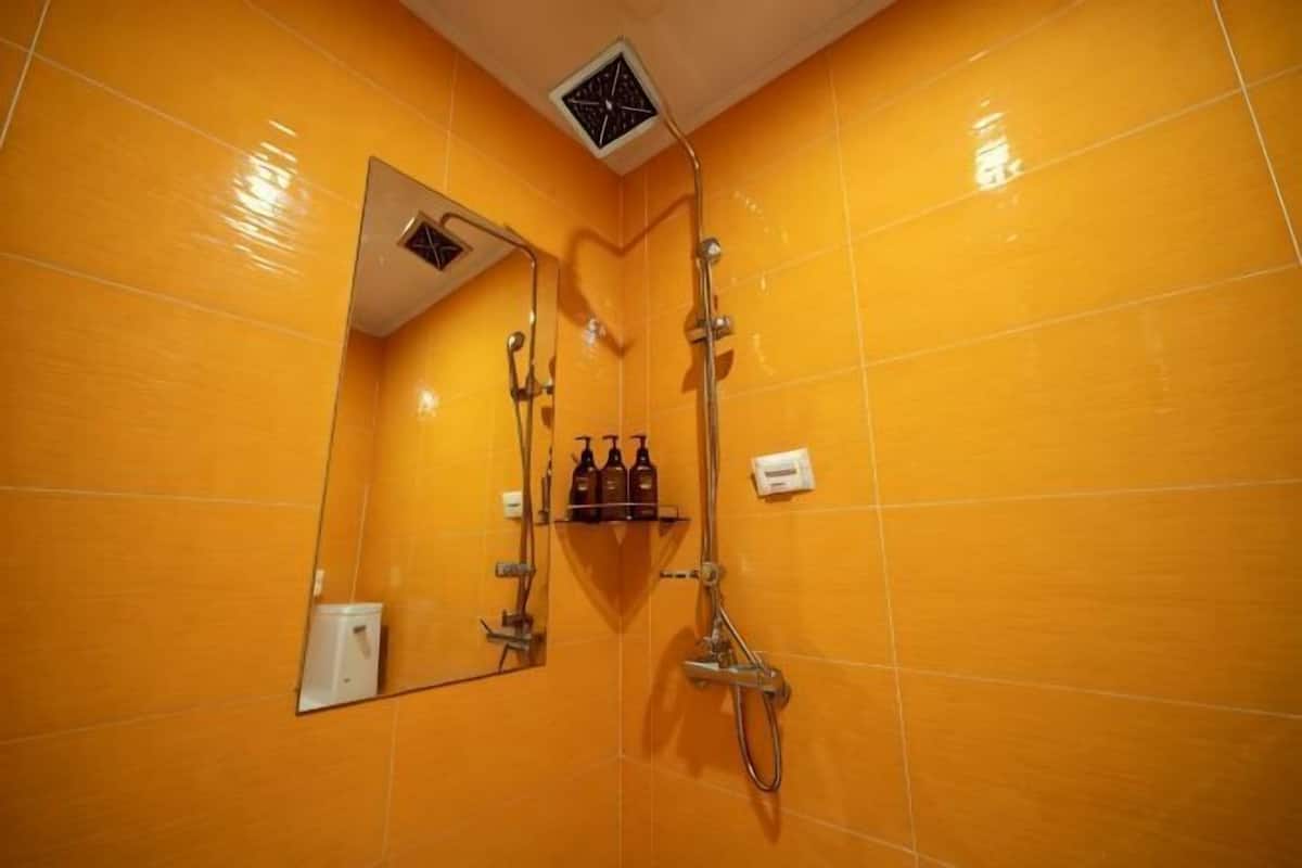 A bathroom with yellow tiles, a shower, a mirror, and a shelf with toiletries.