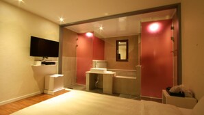 A modern hotel room with a large bed, a flat-screen TV, a small desk with a chair, and a separate bathroom area. - Hotel At noon (Jeju City)