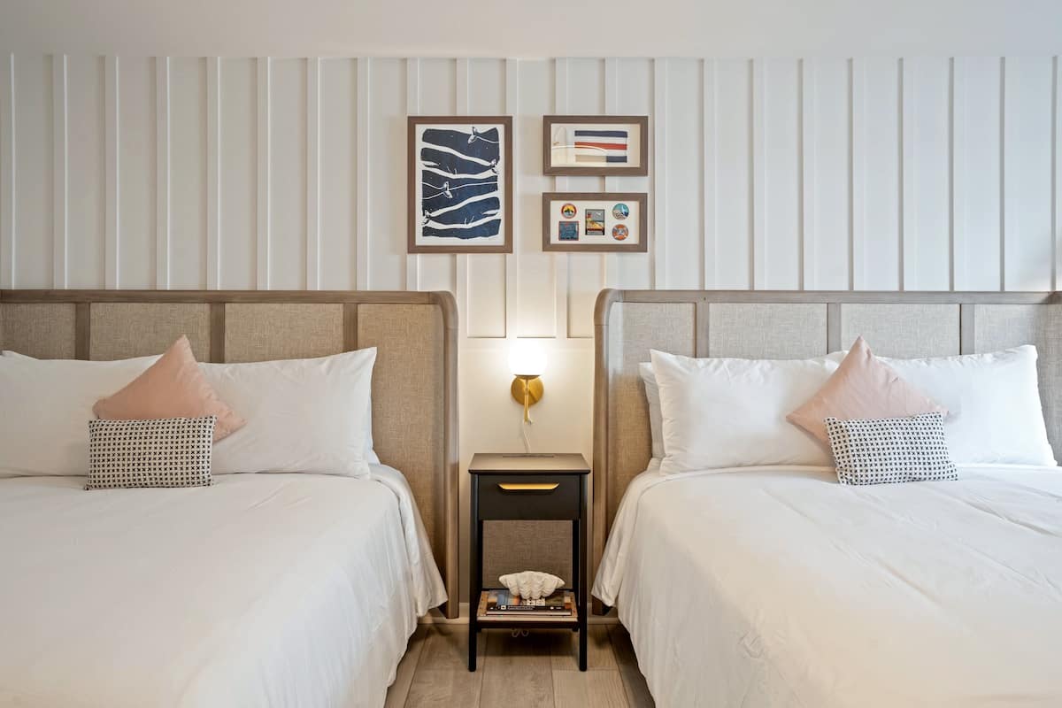 A hotel room with two beds, a nightstand, and wall-mounted artwork.