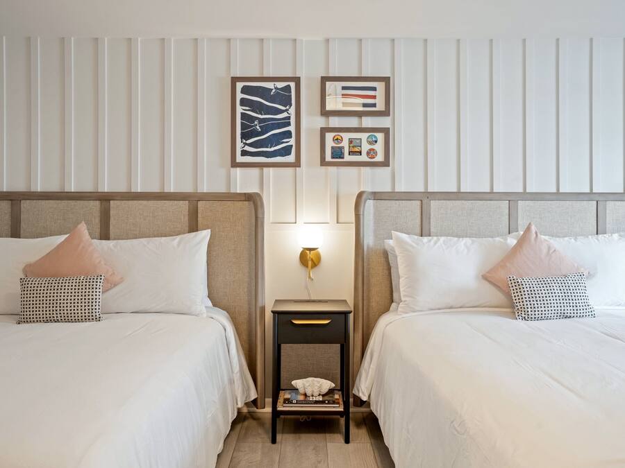 A hotel room with two beds, a nightstand, and wall-mounted artwork.