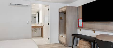 Una habitación de hotel moderna con una cama, un escritorio, una silla, un televisor montado en la pared y un armario.