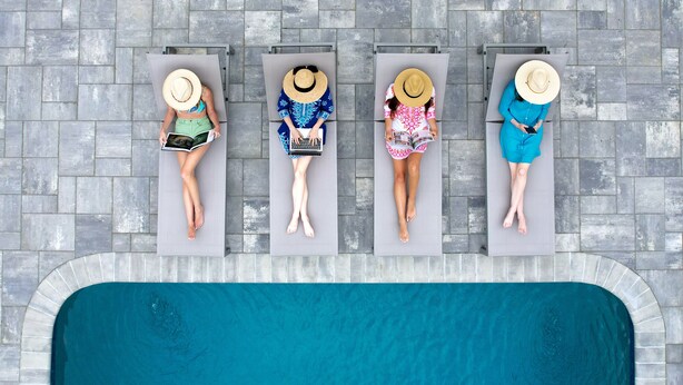 Four sun loungers aligned along a poolside with a tiled floor. - Greyfinch Chatham Inn (Chatham)