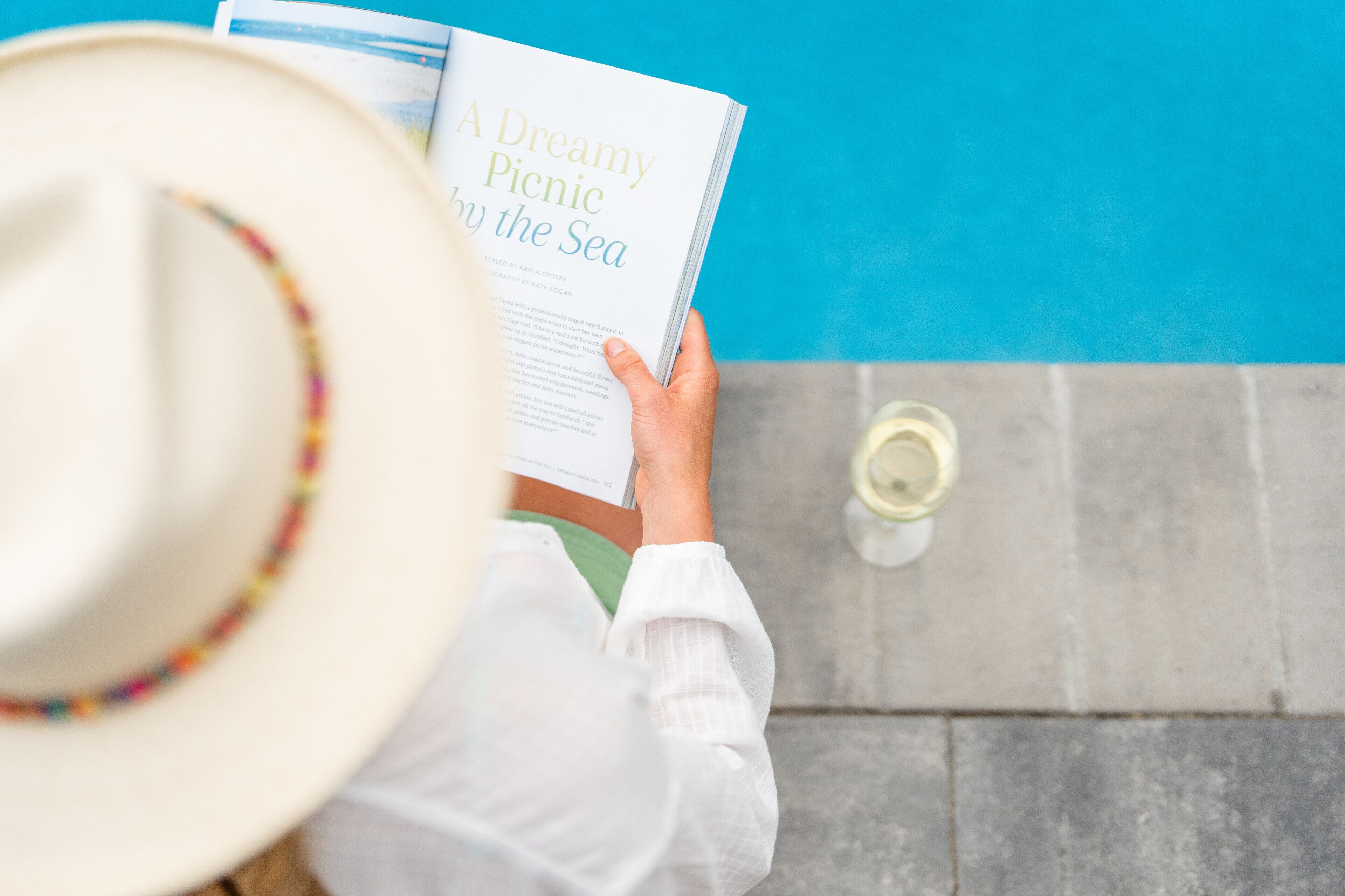 Eine Person liest ein Buch mit dem Titel „Ein träumerisches Picknick am Meer“ in der Nähe eines Pools.