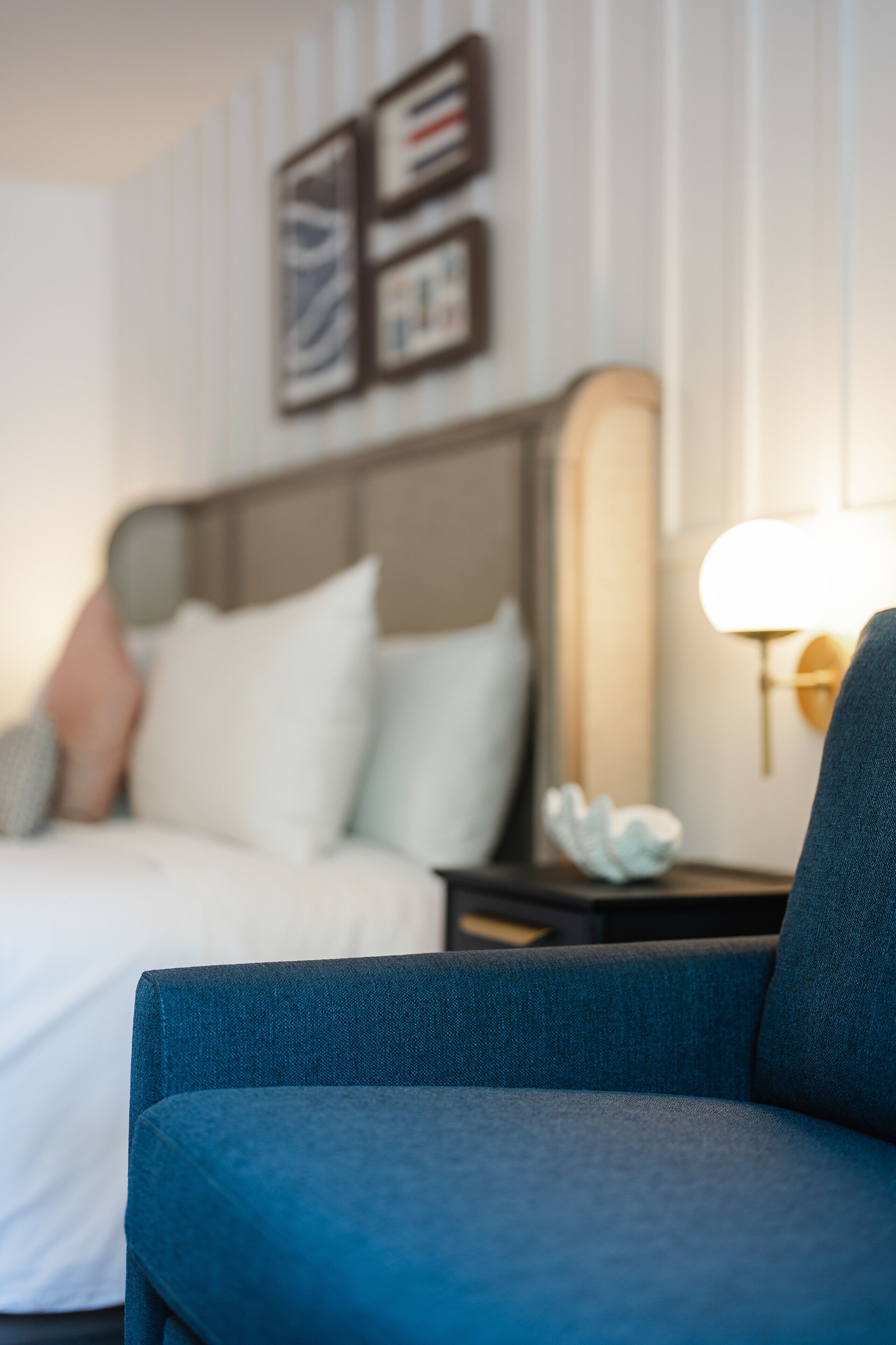 Une chambre d’hôtel avec un lit, une table de chevet, une lampe et un mur orné de tableaux.