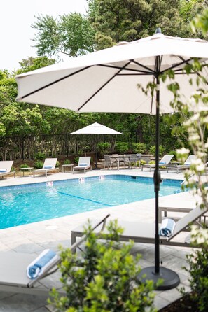 Une piscine entourée de verdure, avec des chaises longues et des parasols.