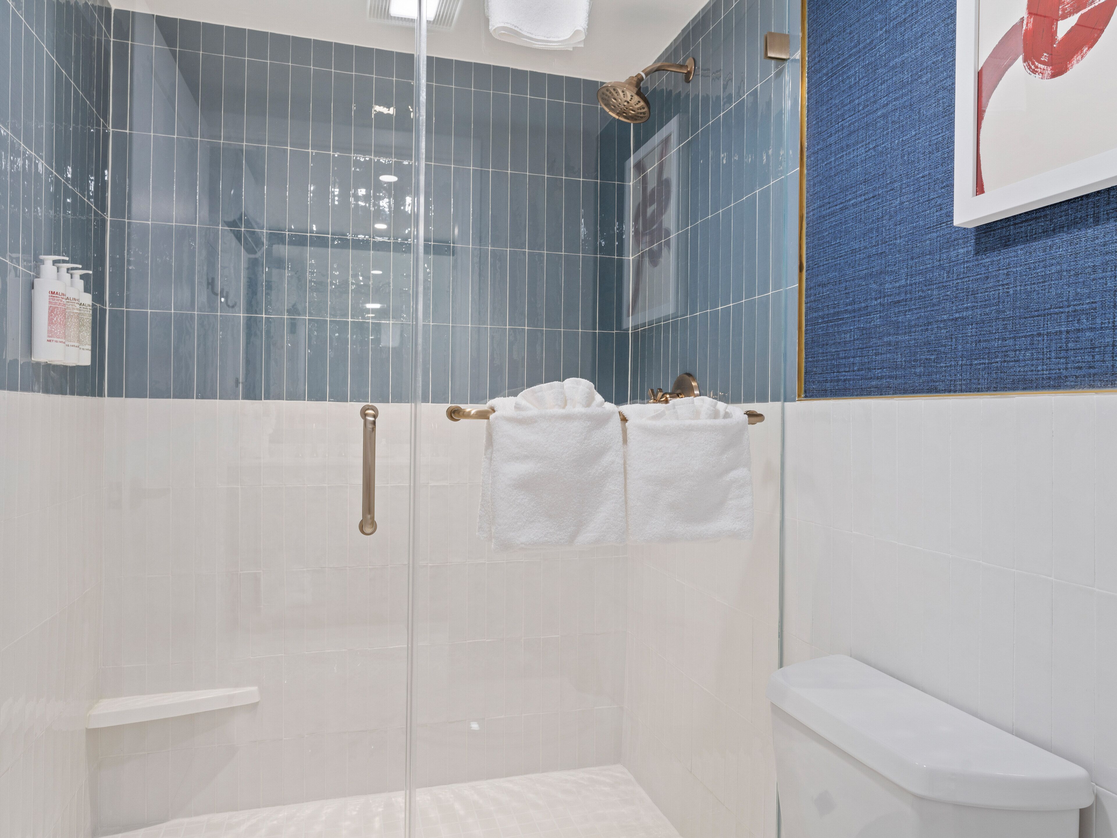 A modern bathroom with a glass shower enclosure, white tiles, a blue accent wall, and a white toilet.
