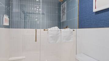 A modern bathroom with a glass shower enclosure, white tiles, a blue accent wall, and a white toilet.