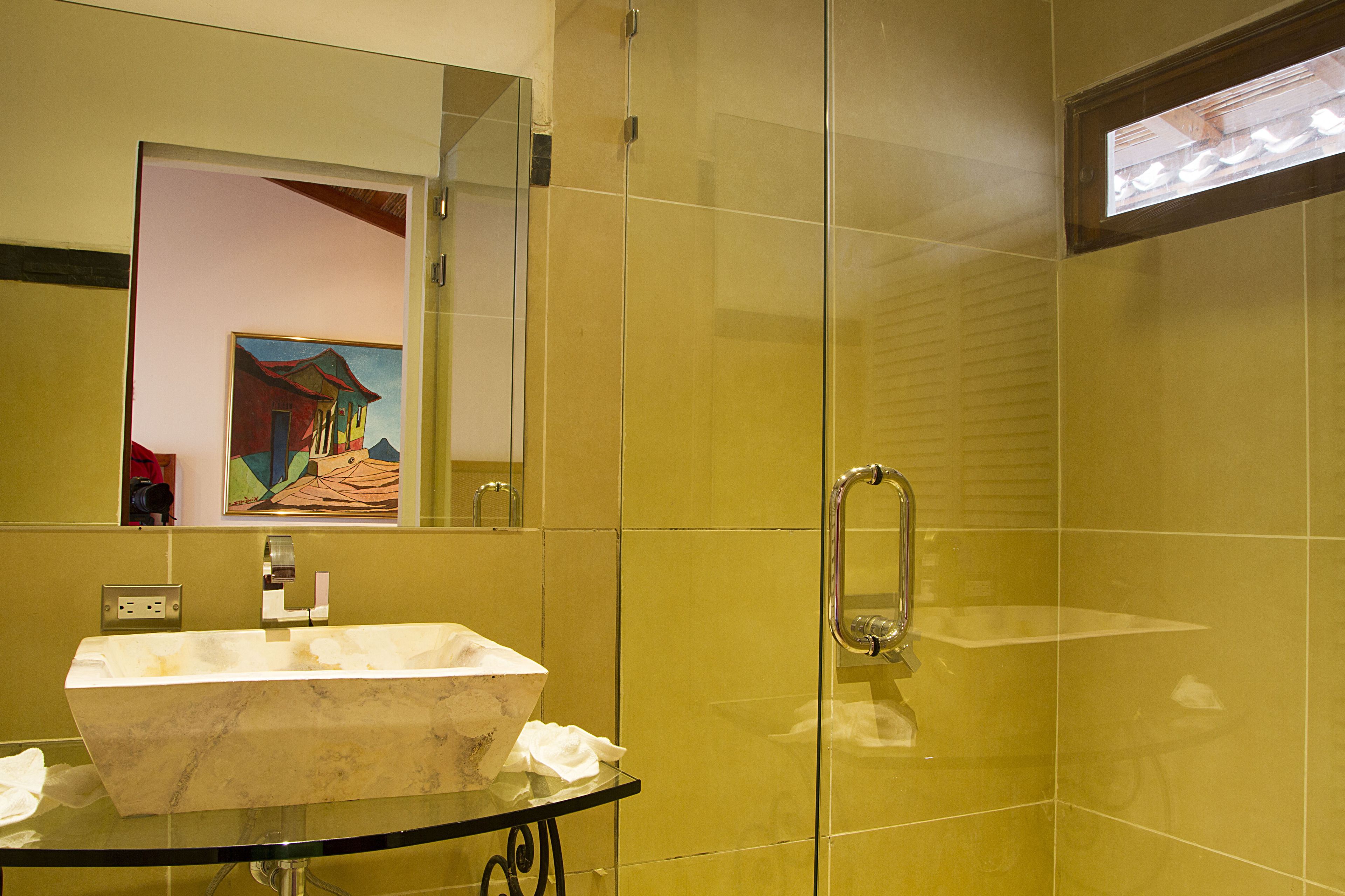 A bathroom with a marble sink, a glass shower enclosure, and a mirror reflecting a painting.