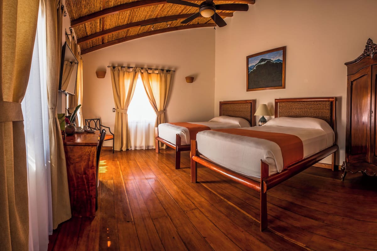 A room with two beds, a wooden wardrobe, a ceiling fan, and a painting on the wall.