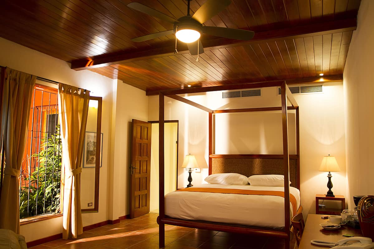 A four-poster bed with a wooden frame, two bedside lamps, and a ceiling fan.