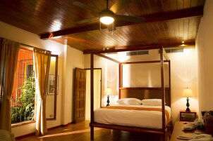 A four-poster bed with a wooden frame, two bedside lamps, and a ceiling fan.