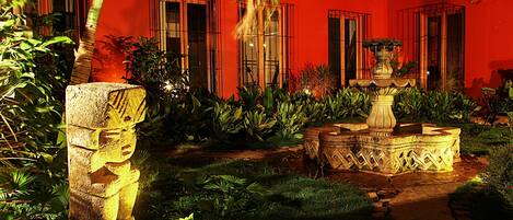 Un patio con una estatua de piedra, una fuente y abundante vegetación.