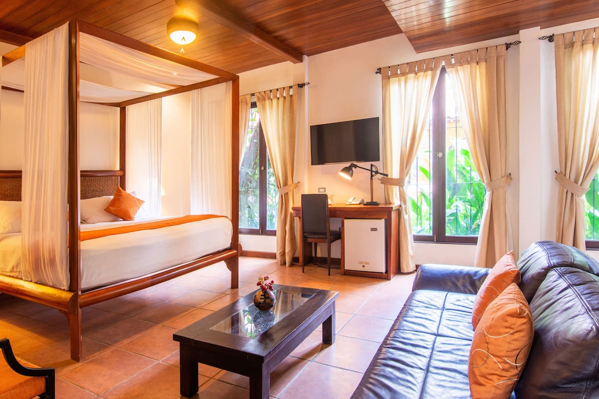 A four-poster bed with a desk and a sofa in a well-lit room with large windows.