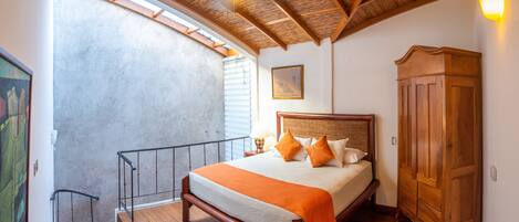A bedroom with a wooden bed, a wardrobe, a balcony with a railing, and a ceiling with wooden beams.