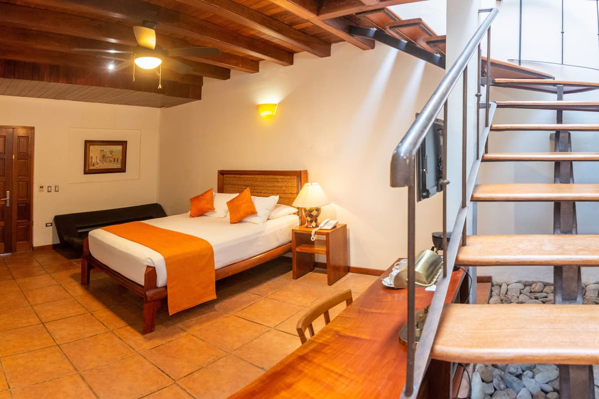 A bedroom with a wooden bed, a nightstand, a lamp, and a staircase.