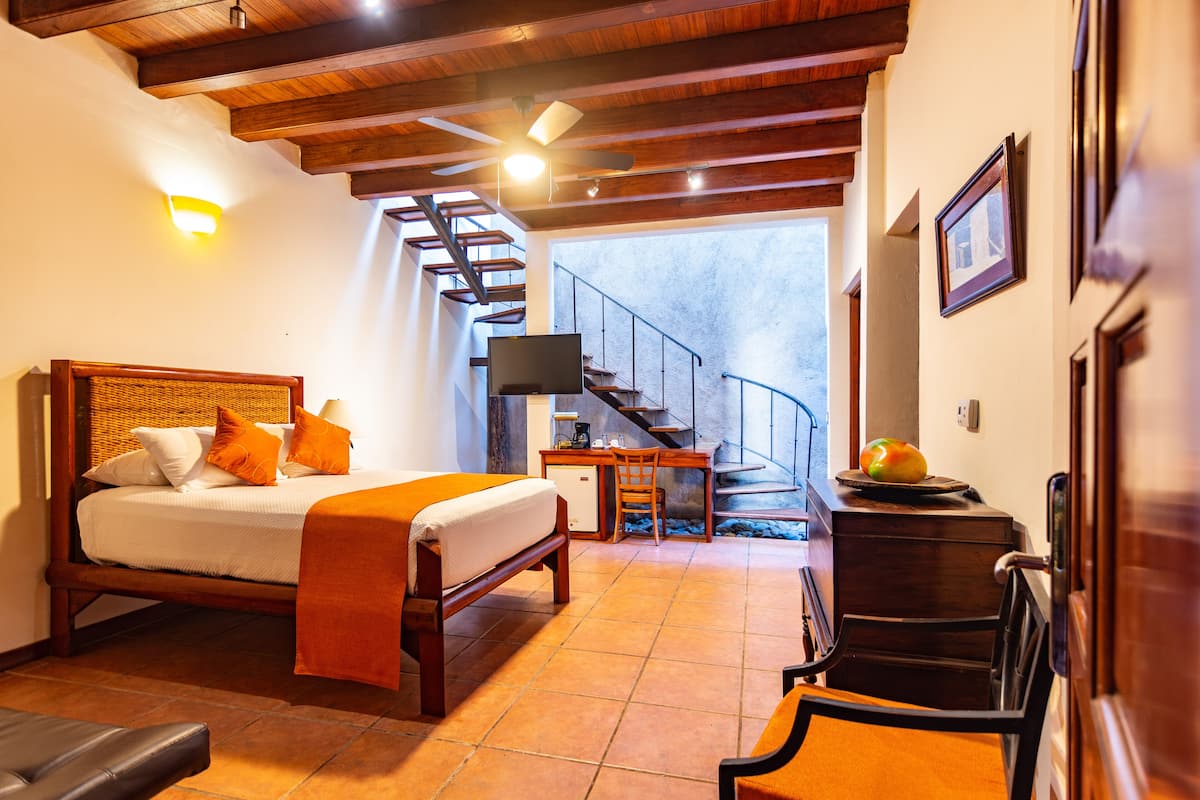 A bedroom with a bed, a desk, a chair, a TV, and a staircase leading to an upper level.