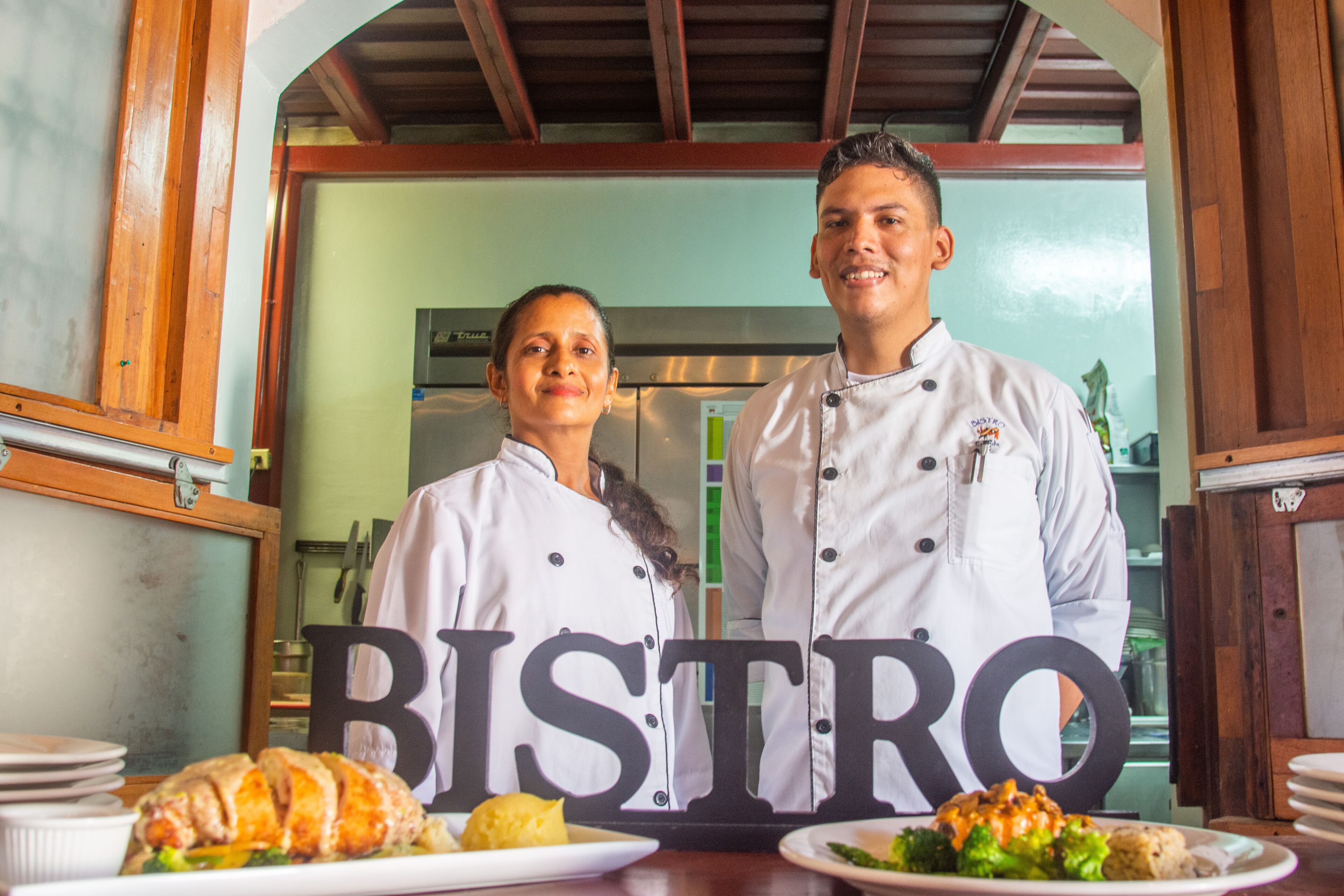 Um bistrô com interior em madeira, um letreiro grande com a palavra 'BISTRO' e pratos de comida no balcão.