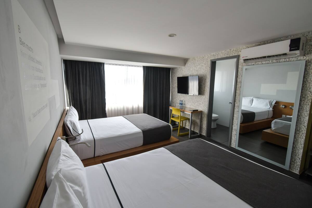 Ett hotellrum med två sängar, ett skrivbord, en stol, en TV och ett badrum.