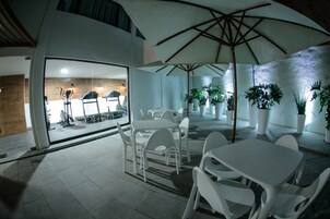 A modern outdoor dining area with white plastic chairs and tables, large umbrellas, and potted plants.