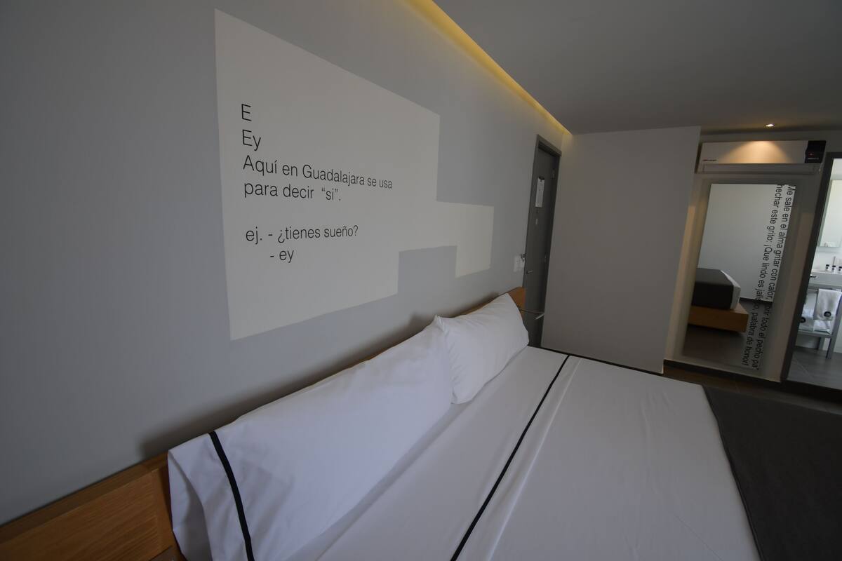 Ett hotellrum med en säng, en väggmonterad skärm som visar text och en dörr som leder till ett annat rum.