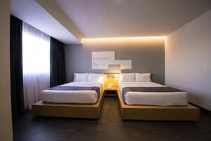 A modern hotel room with two beds, a bedside table, and a wall-mounted light fixture.