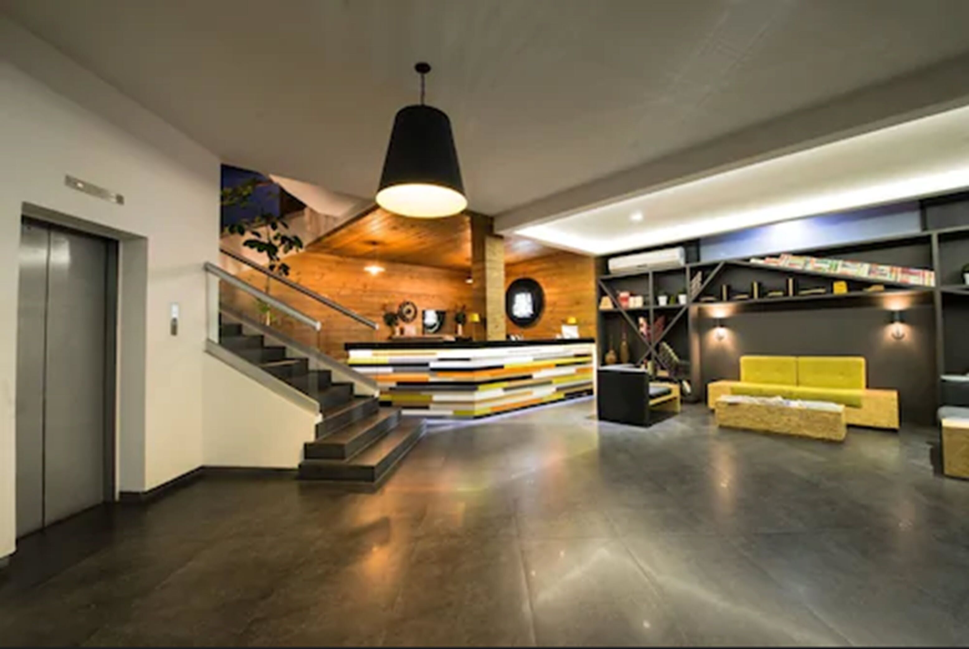 A modern lobby with a staircase, a reception desk, and a yellow sofa.