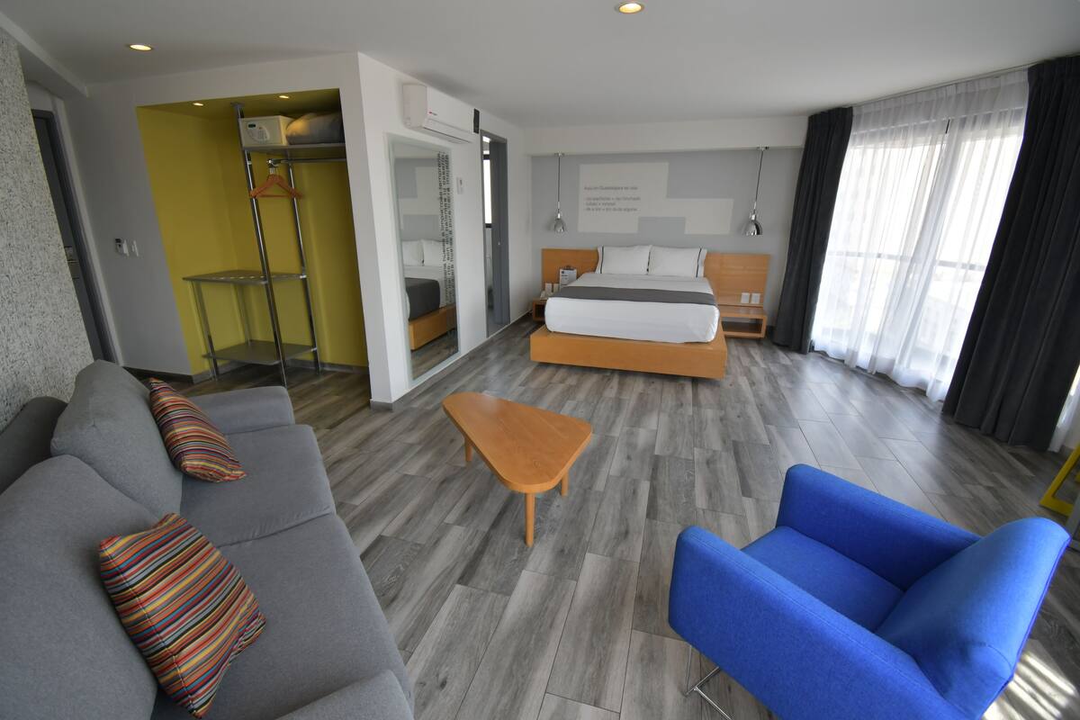 Ett hotellrum med en säng, en soffa, en stol, ett litet bord och en garderob.