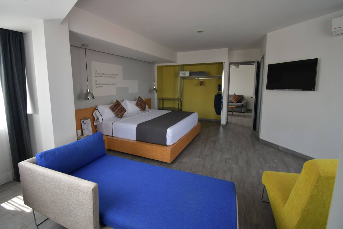 Ett modernt hotellrum med en stor säng, en blå soffa, en gul fåtölj och en tv på väggen.