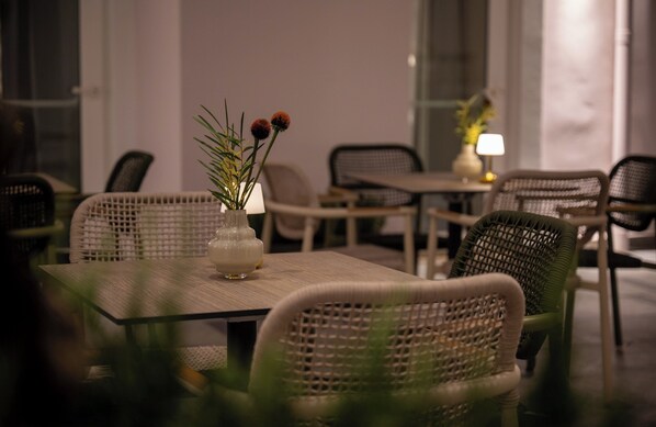 Un coin repas avec des chaises et des tables en osier, un vase rempli de fleurs et une lampe posée sur une table d’appoint.