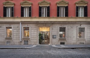 A building facade with a large entrance, multiple windows with shutters, and a sign indicating a boutique hotel. - Leonardo Boutique Hotel Rome Monti (Rome)