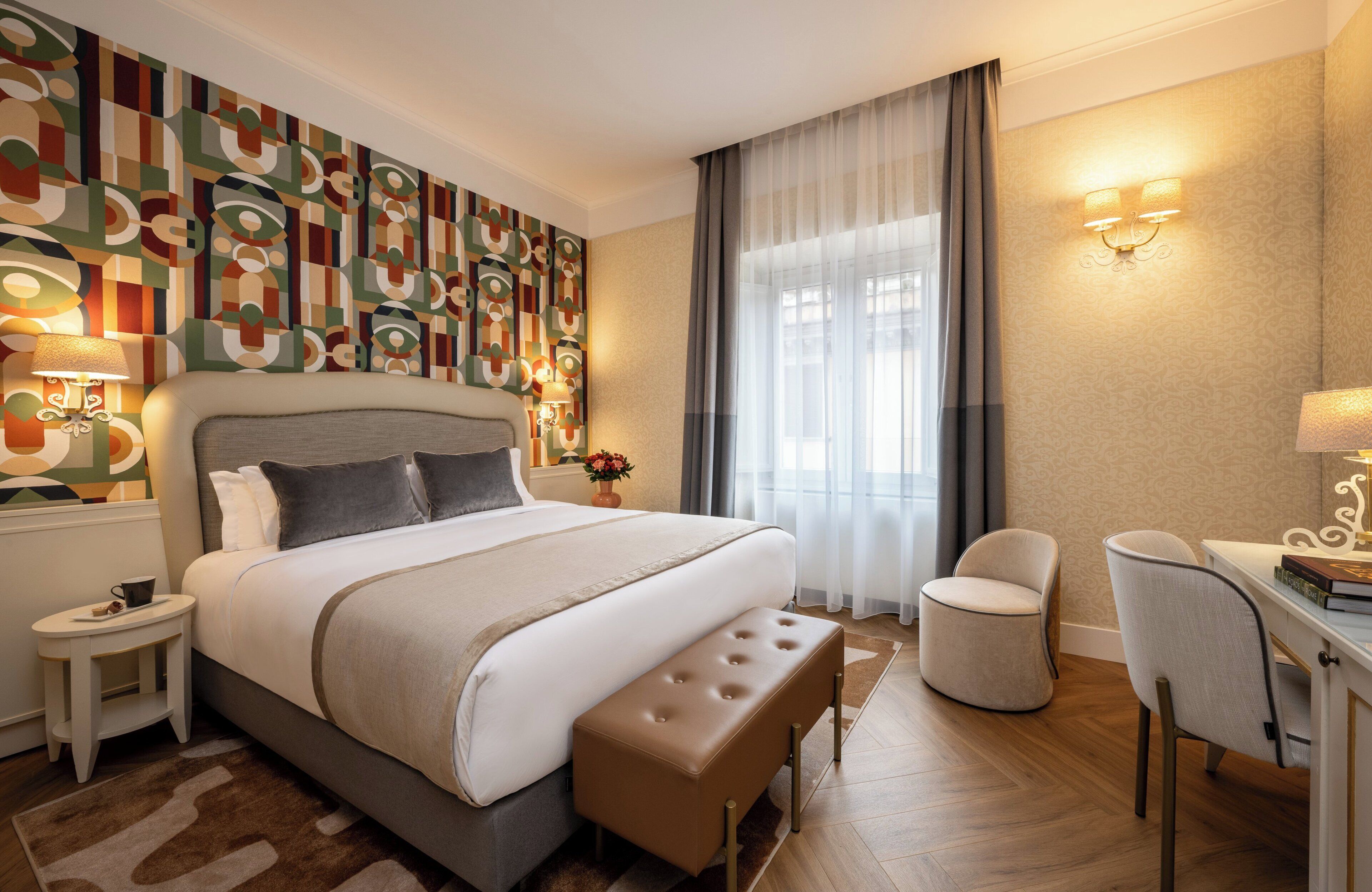 A modern hotel room with a large bed, a desk, a chair, and a decorative wall.