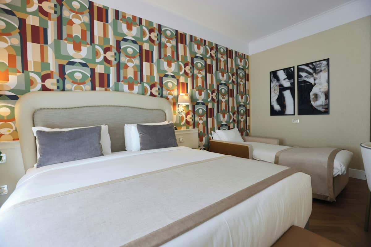 A hotel room with a large bed, two bedside tables, a nightstand, and a wall with abstract art.