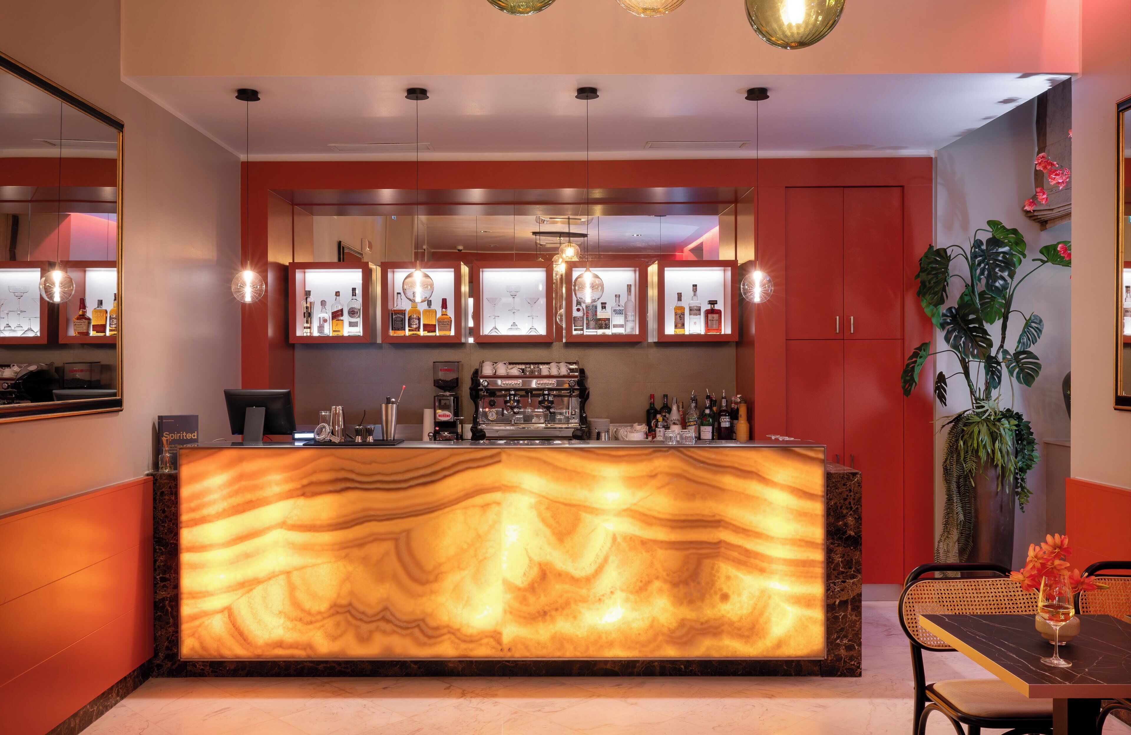 A bar area with a marble countertop, shelves with bottles, and hanging pendant lights.