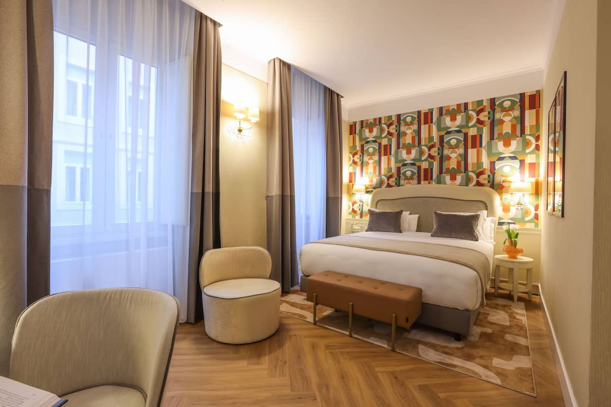 A hotel room with a large bed, a round armchair, a small table, and a decorative wall.