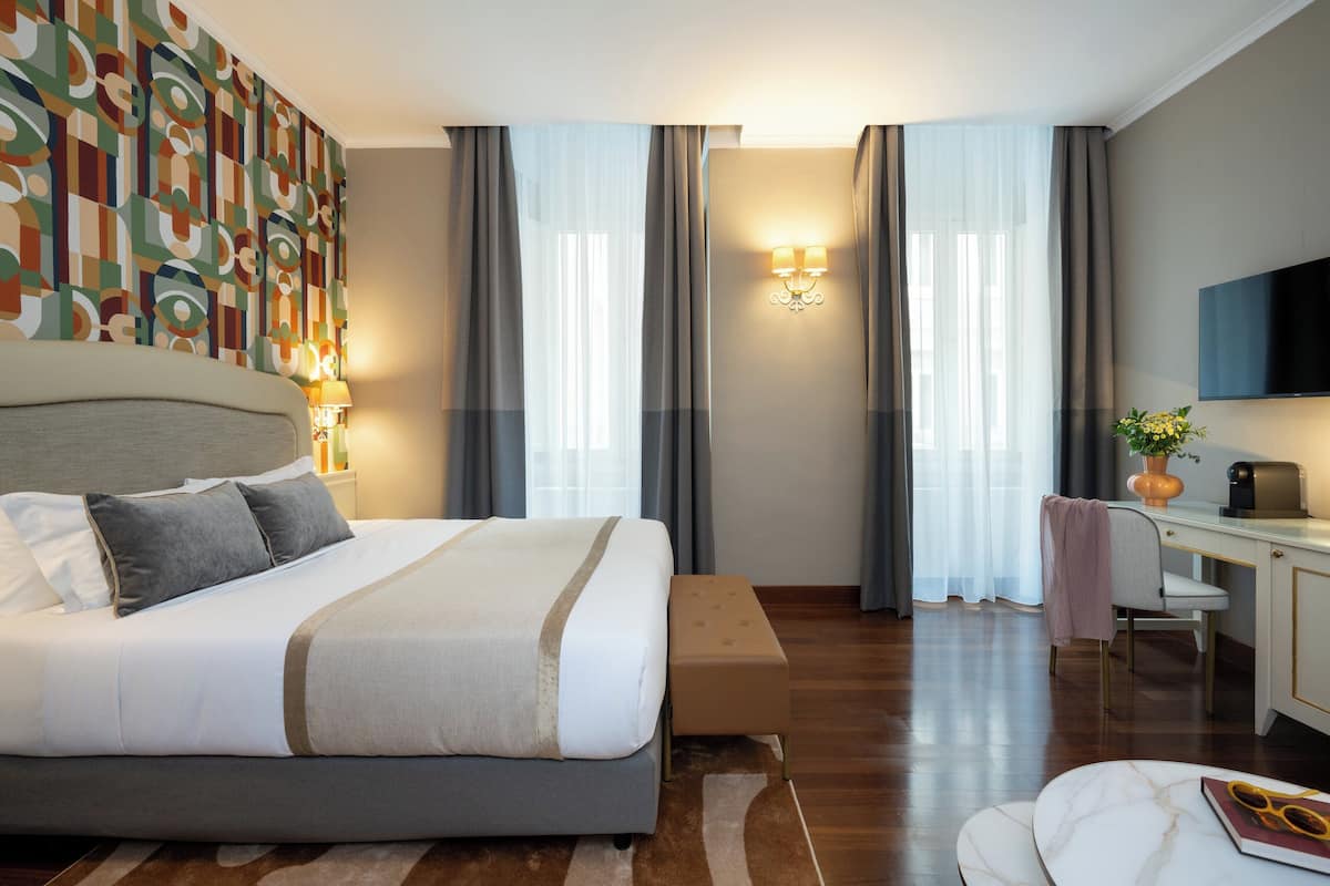 A modern hotel room with a large bed, a desk, a TV, and a view of the city.