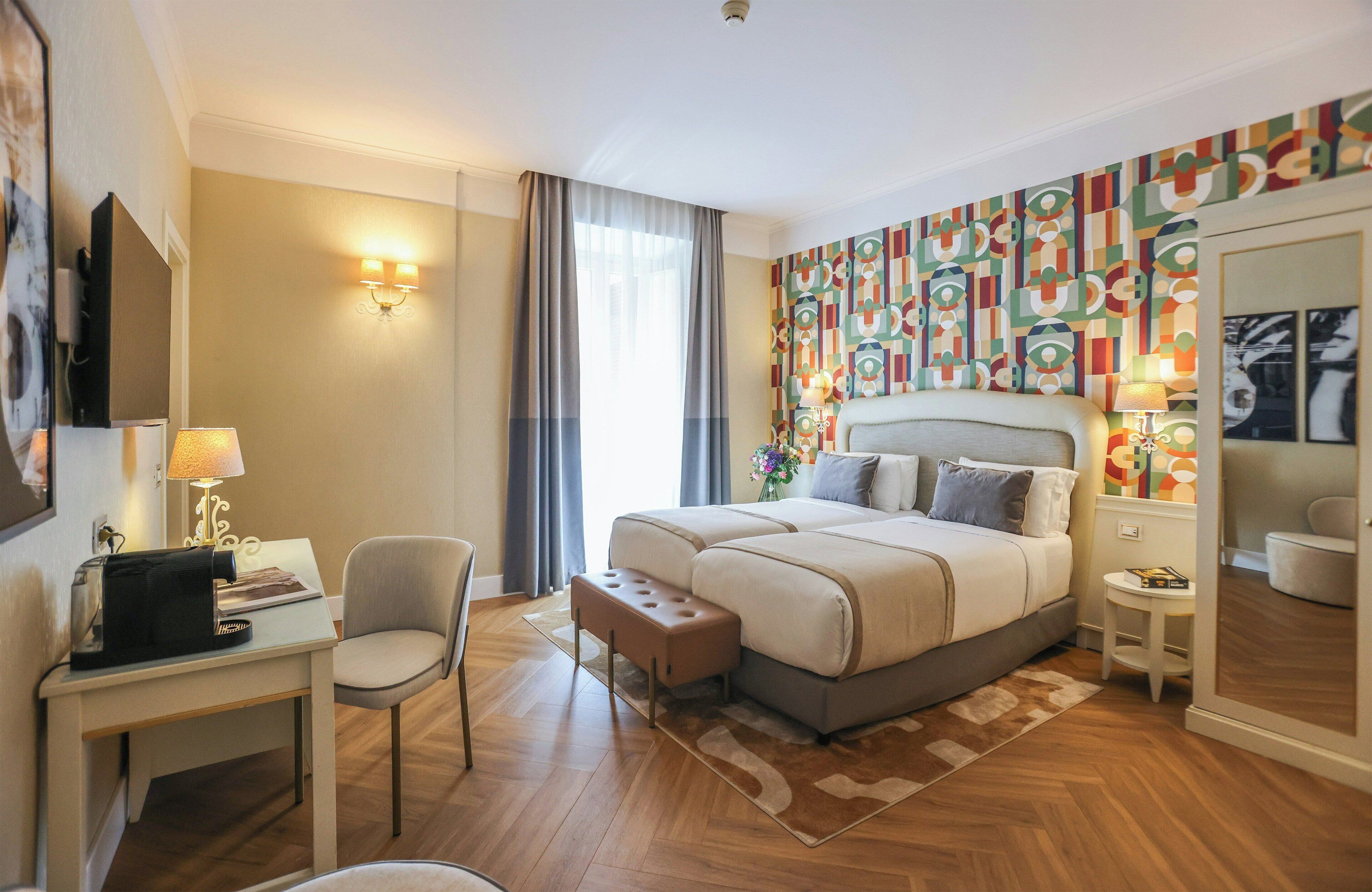 Habitación de hotel con una cama grande, un escritorio con lámpara, una silla y una mesita.