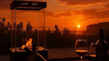 A sunset view from a balcony with a fire feature and wine glasses.