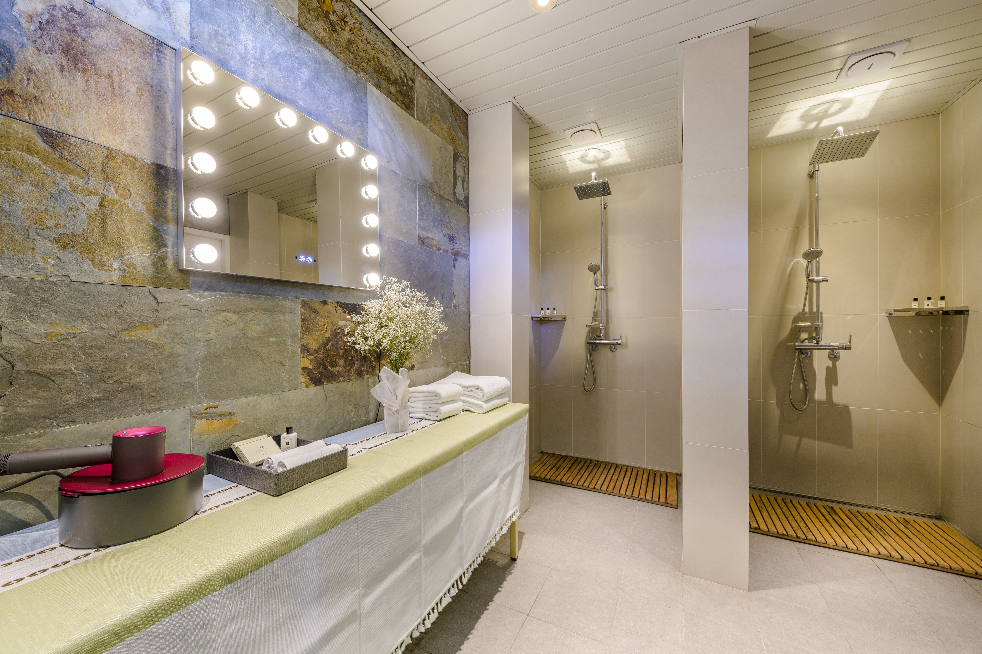 Een badkamer met een wastafel, een spiegel met verlichting, een douche en een stenen muur.