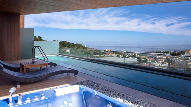 A modern outdoor pool area with a wooden deck, lounge chairs, and a hot tub. - Bayhill Pool & Villa (Seogwipo)