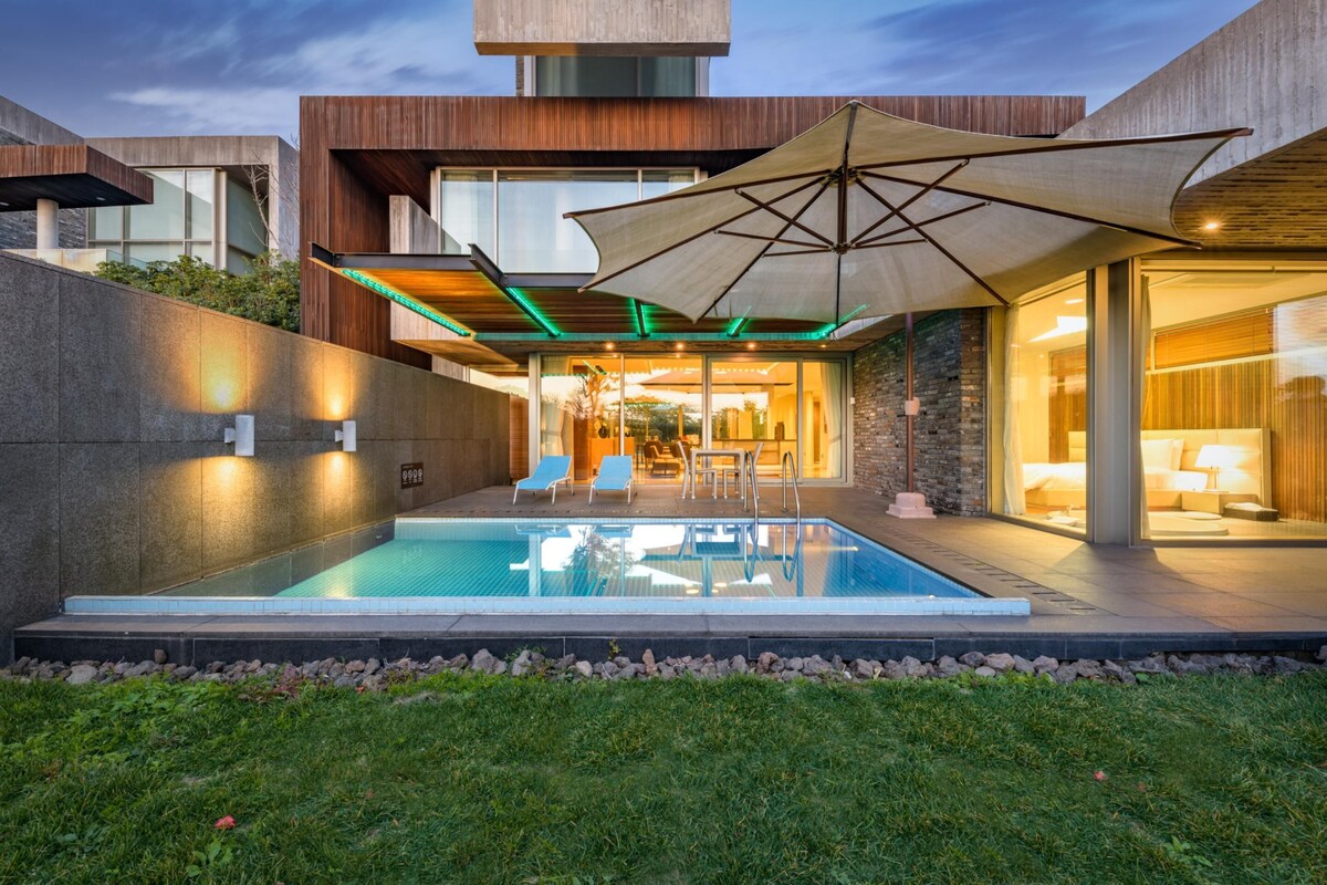 A modern house with a swimming pool, outdoor seating, and a large umbrella.