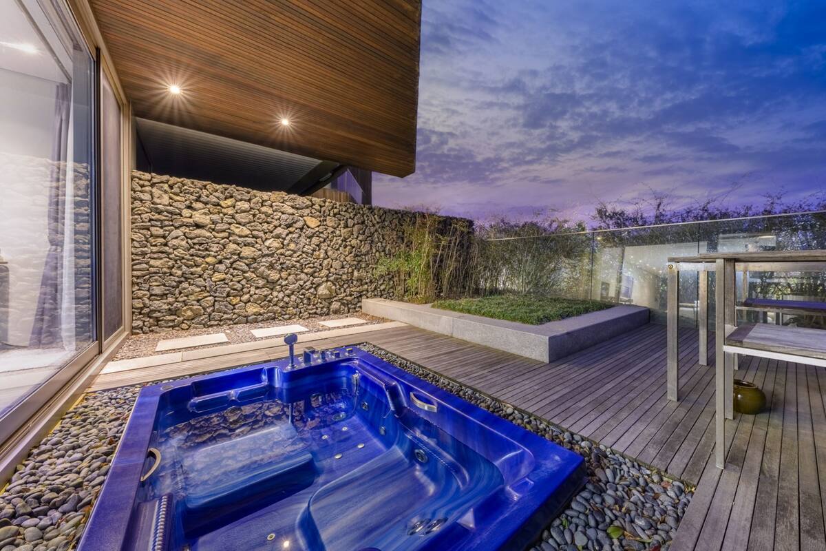 A modern outdoor hot tub area with a stone wall and wooden deck.