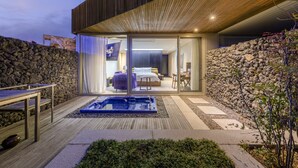 A modern outdoor living area with a hot tub, stone walls, and a wooden deck. - Bayhill Pool & Villa (Seogwipo)